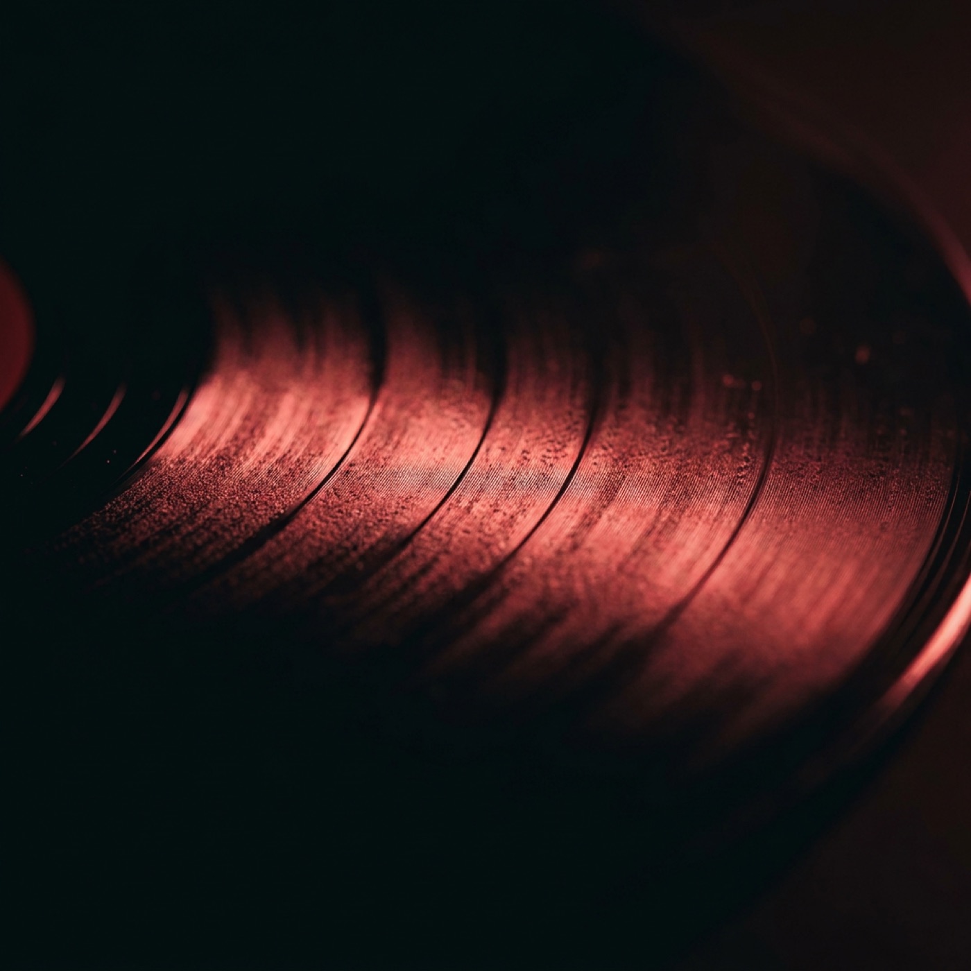 A black vinyl record catching a single shaft of red light